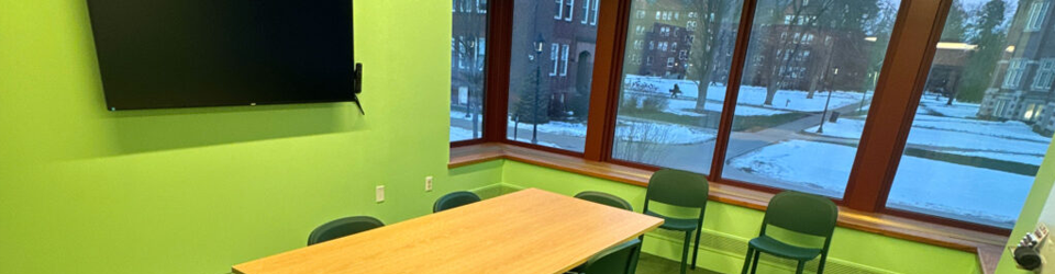 Study room with green walls, a table, green chairs, whiteboard, and a television for screen sharing.